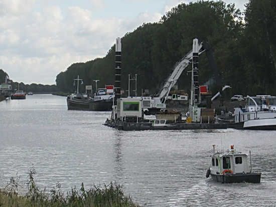 Hier is het wat beter te zien. Bagger wordt in een gereedliggende schuit gehesen, een tweede lege boot ligt al weer klaar. Een motorboot van Waterstaat bekijkt de situatie op de voorgrond.