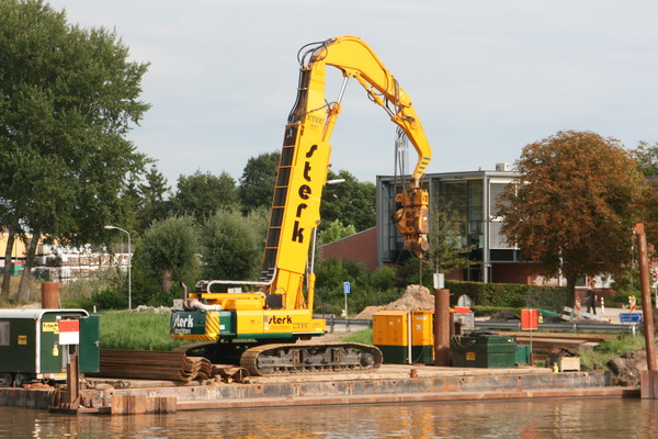 De STERK-kraan op de ponton aan de zuidkant van het kanaal. De scheepvaart kan nauwelijks gehinderd passeren. Op het het grote vlot liggen de gegolfde platen al klaar die zaterdagavond 14 september voor de damwanden werden gebruikt.
