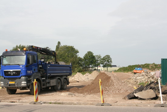 Hier staat de betrokken vrachtauto, brokstukken van het plaveisel verplaatsend. Op de achtergrond het tracé van de aan te leggen omleidingsweg.