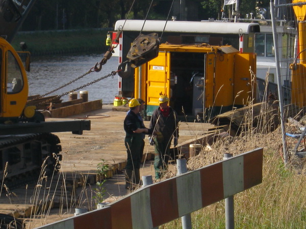 Drie betrokkenen in overleg, in discussie, in gesprek in ieder geval. Twee met een helm (van Sterk), de derde zonder. Stel dat er een vogel overvliegt....