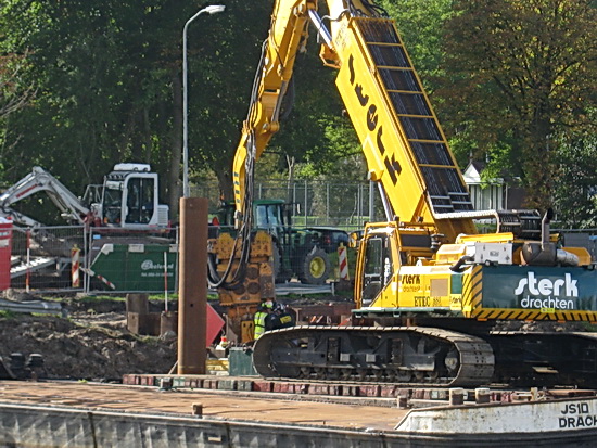 Verder inzoomen levert niet veel meer duidelijkheid op. Platen uit de grond, platen in de grond... IJzeren balken aan de zijkant.... En bij de weg een kleine grijper die waarschijnlijk ingezet wordt om de aansluiting van de leiding mogelijk te maken.