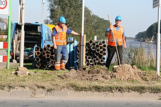 Even afstand genomen van het directe tunnelterrein, bij de brug twee andere "ingehuurden" die bezig zijn 'slangen" in een sleuf onder te brengen. "Nee, niet onder de weg door, maar langs de weg naar de tunnel!" verklaart de ene. "Voor toevoer van water, de tunnelwand moet waterdicht worden gemaakt en daarvoor is water nodig..." "O..." "Acht", zegt de ander, "Hoe het precies zit? Wij zijn hier om ons werk te doen, niet om na te denken..." 