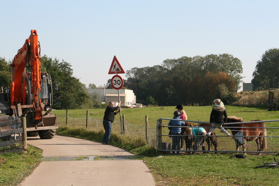 De draglinebestuurder vindt het welletjes. Hij plaatst de verkeersborden weer op de goede plek: Werk in Uitvoering en Maximaal 30 km. Mooi zo!