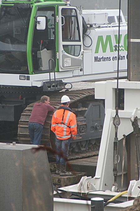 De super baggeraar is hier nog in afwachting van de bevindingen van het peilteam: Moet er nog weer worden gebaggerd of niet? De gehelmde contactman houdt hem gezelschap, bemoedigend. 