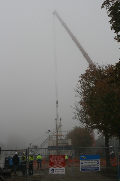 Het afgeschermde werkterrein met een dubbele waarschuwing: Er is cameratoezicht en bezoekers, melden bij de GMB-opzichter! Welke van al die helmen zou dat zijn?