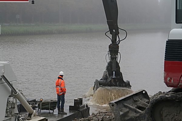De contactman op het werkeiland, oranje jas, witte helm, slaat het hernieuwde baggeren gade. 'Als het nou maar de laatste keer is....'