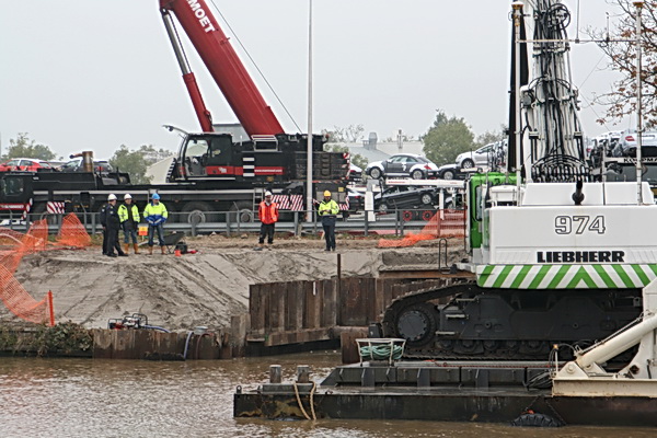 Zo kun je de noordelijke werkplek observeren vanaf de zuidelijke oever. De zon breekt door, de belichting wordt beter. Nog steeds helmen en hesjes niets doende, handen in de zakken. Watcher Ep Homan is het een doorn in het oog....