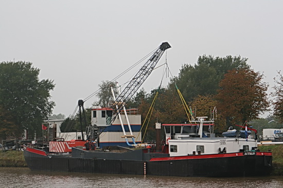 De kraanboot "Redbad" waaraan het linker deel van de tweelingbuizen is bevestigd. Het schip gaat, als het "Ja, het kan!" heeft geklonken, naar de zuidoever varen, zodat de buizen over het kanaal komen te liggen. Het noordeinde neemt de mammoetkraan van Wagenborg voor zijn rekening.