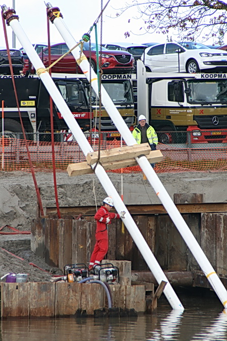De man in rode overall en witte helm weet precies op welke punten hij de kettingen van de kraan dient te bevestigen om het gewenste resultaat te behalen. Hopen dat het hem lukt.....