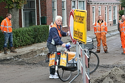 De PostNL-besteller ongewild in het centrum van de belangstelling. Komt er net een grote grijper aanrijden, zet zij doodnuchter de postfiets in de gevarenzone: "Ja, ik moet mijn werk ook doen!"